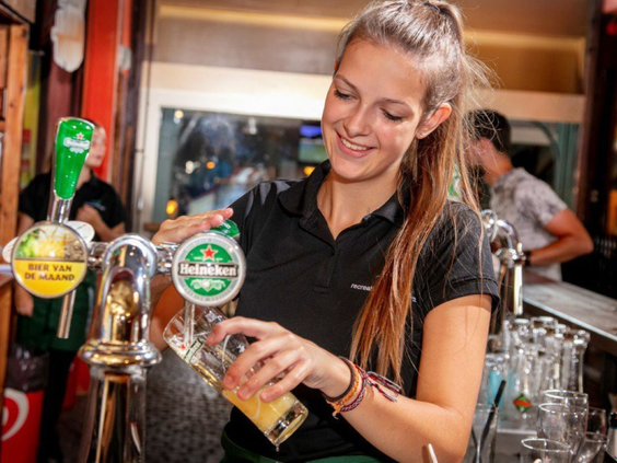 Vriendelijke medewerker tapt een drankje achter de bar in het restaurant van Vakantiepark De Bergen.