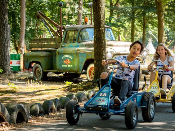 Kinderen hebben plezier tijdens het rijden op skelters op de avontuurlijke skelterbaan in het bos.