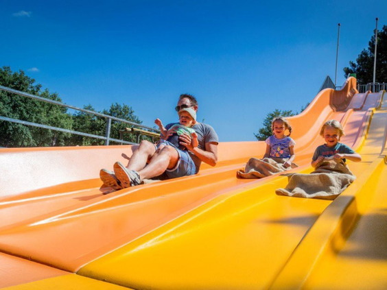 Vader met zijn kinderen glijdt van de brede, oranje familieglijbaan bij Vakantiepark De Bergen.