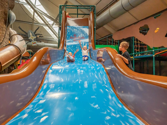 Kinderen glijden van een grote blauwe glijbaan in de binnenspeeltuin de Holle Bolle Boom