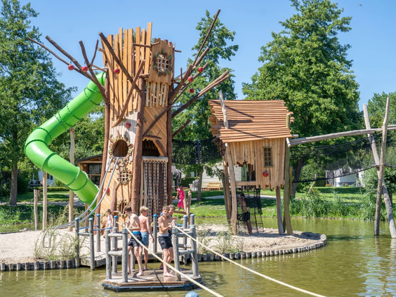Een hoge houten klimtoren met een groene glijbaan in de buitenspeeltuin