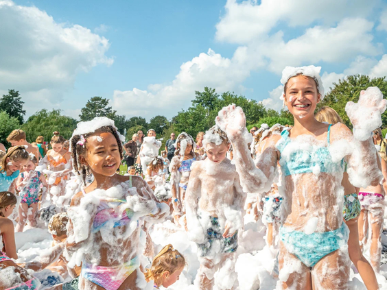 Kinderen dansen in de witte wolken tijdens een schuimparty op de camping