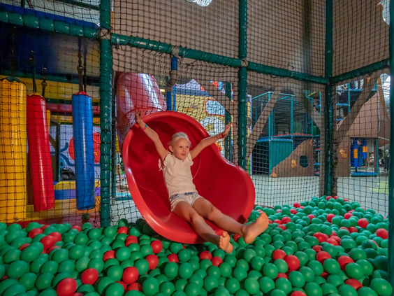 Een kind glijdt in de grote ballenbak vol gekleurde ballen