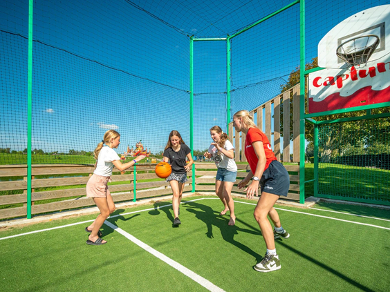 Meisjes spelen een fanatiek potje basketbal op het kunstgras sportveld.
