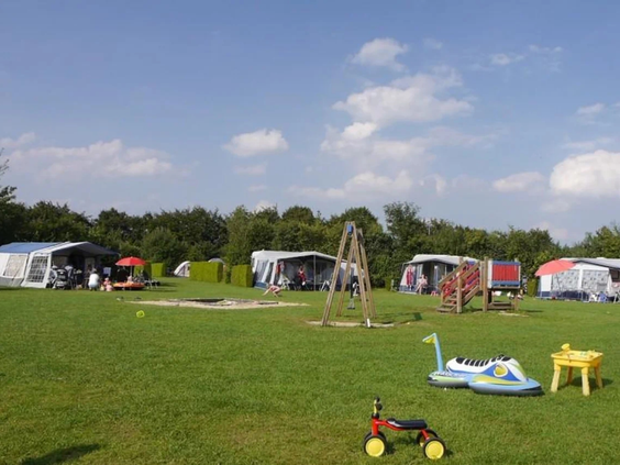 Een weids uitzicht over een groen kampeerveld met tenten en caravans