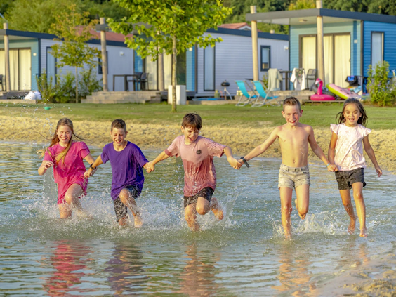 Groepje kinderen rent lachend door het ondiepe water bij de zwemvijver