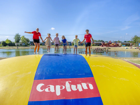 Kinderen springen op de grote gele airtrampoline bij de zwemvijver