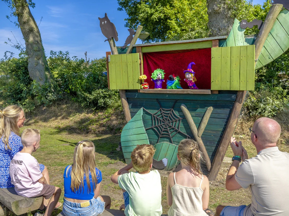 Kinderen kijken ademloos naar een poppenkastvoorstelling in de buitenlucht