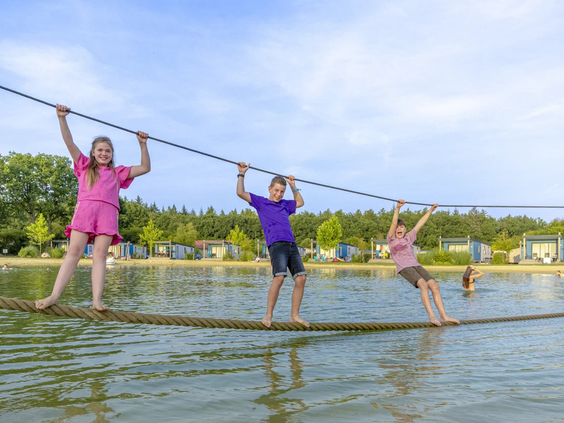 Kinderen lopen over een wiebelige touwbrug boven het water van de vijver