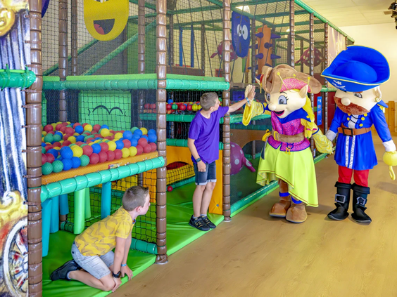 Kinderen spelen bij een klimtoestel in de binnenspeeltuin met een mascotte