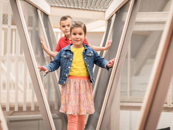 Twee kinderen, een jongen en een meisje, spelen vrolijk op een moderne houten loopbrug bij Vakantiepark De Krim op Texel.