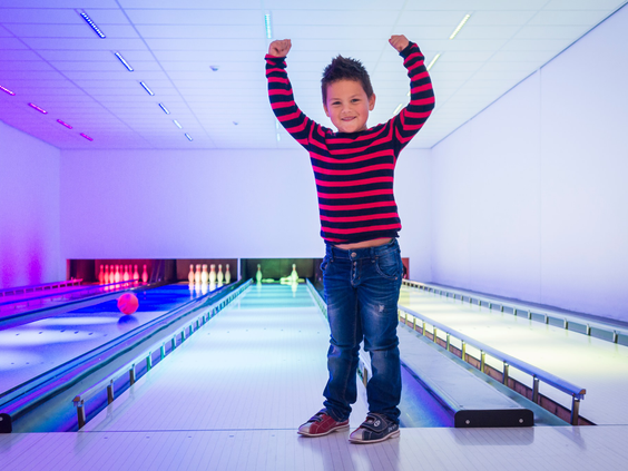Een jongen juicht enthousiast op de kleurrijk verlichte bowlingbaan van Vakantiepark De Krim op Texel.