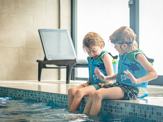 Twee jongens met zwemvestjes en duikbrillen zitten met hun voeten in het water aan de rand van het binnenzwembad van Vakantiepark De Krim.