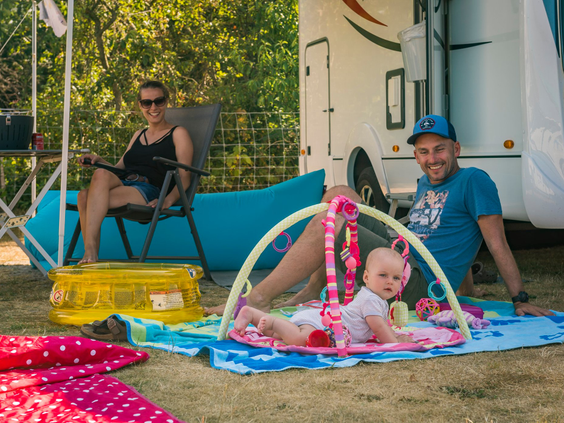Ouders ontspannen bij hun camper terwijl hun baby op een speelkleed speelt op de camping van Vakantiepark De Krim Texel.
