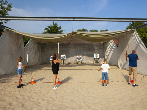 Kinderen leren boogschieten onder begeleiding van het animatieteam op de camping