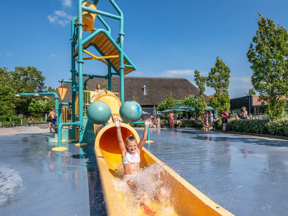 Kinderen glijden tegelijk van de brede gele glijbaan in het waterpark