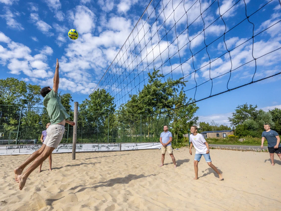 Jongeren spelen een potje beachvolleybal op het zandveld van de camping
