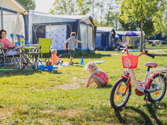Kinderen op de fiets op een zonnig kampeerveld tussen de caravans