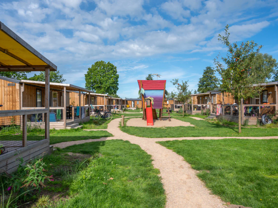 Een rij moderne vakantielodges en chalets langs een groen en bloemrijk pad