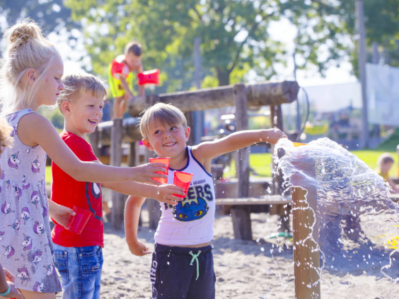 Kinderen spelen met houten waterpompen en watergoten in de natuurspeeltuin