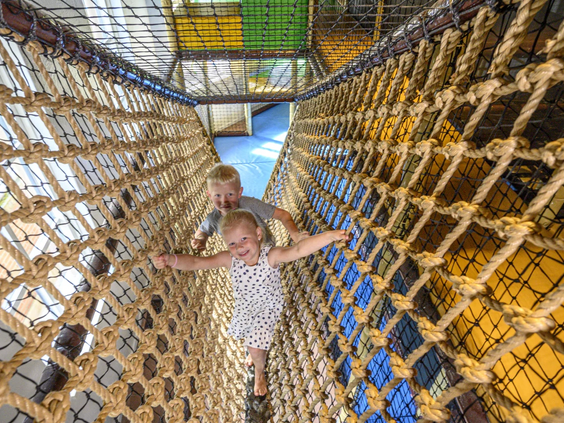 Kinderen klimmen in de uitdagende indoor klimnetten van de binnenspeeltuin
