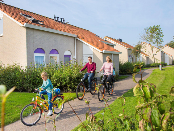 Een gezin fietst vrolijk tussen de vakantiehuizen op Vakantiepark De Soeten Haert in Renesse.