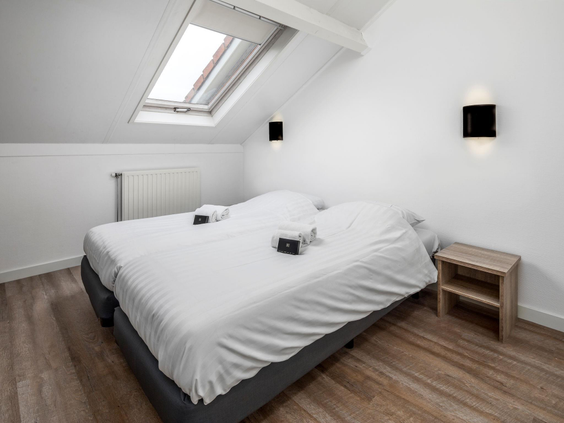 Een nette slaapkamer met een tweepersoonsbed onder een schuin dakraam in een vakantiehuis op De Soeten Haert.