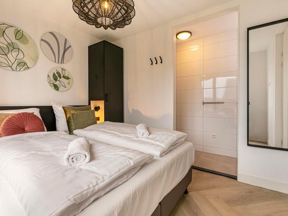 Een luxe ingerichte slaapkamer met een opgemaakt tweepersoonsbed en een en-suite badkamer in een vakantiewoning op De Strabrechtse Vennen.
