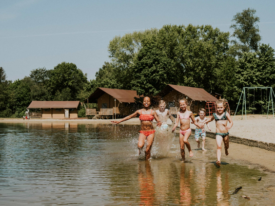 Een groep kinderen rent en spettert in het ondiepe water van de recreatieplas op Vakantiepark Dierenbos.