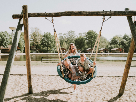 Moeder en twee kinderen op grote nestschommel bij strand en zwemvijver van Vakantiepark Dierenbos