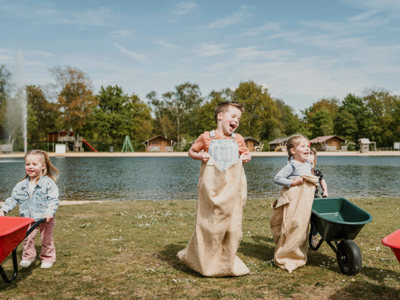 Kinderen doen mee aan een potje zaklopen op het grasveld bij de recreatieplas, georganiseerd door het animatieteam van Vakantiepark Dierenbos.