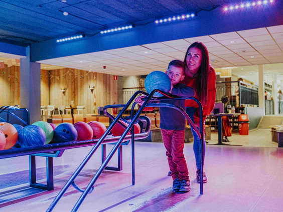 Een moeder helpt haar zoontje met het gooien van een bowlingbal op de sfeervolle bowlingbaan van Vakantiepark Dierenbos.