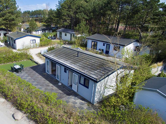 Luchtfoto van een vrijstaand chalet met een eigen terras en tuinmeubilair, gelegen tussen het groen op Roompot Vakantiepark Egmond aan Zee.