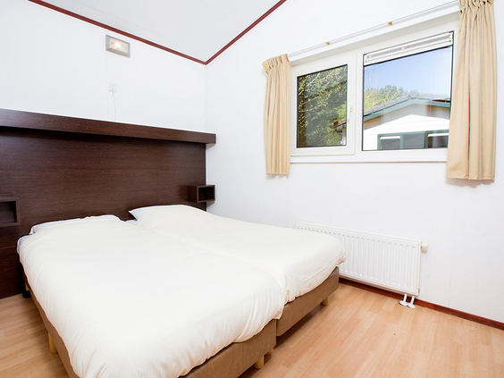 Nette slaapkamer in een chalet op Vakantiepark Egmond aan Zee, met twee comfortabele, opgemaakte eenpersoons boxspringbedden en een raam.
