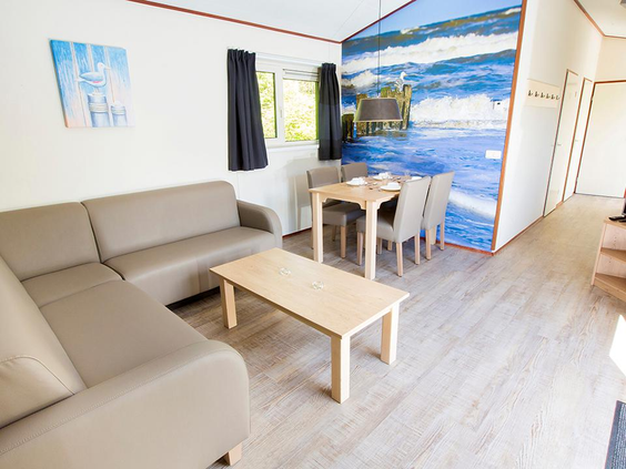 De woonkamer van een chalet op Vakantiepark Egmond aan Zee met een comfortabele hoekbank, eethoek en een opvallende fotowand met een afbeelding van de zee.