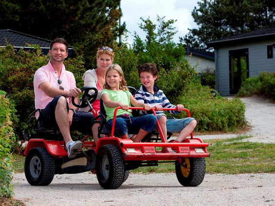 Een vrolijk gezin met twee kinderen maakt een rondje over het park op een grote rode familieskelter bij Vakantiepark Egmond aan Zee.