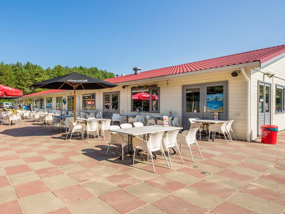 Het ruime, zonnige terras van het restaurant op Vakantiepark Egmond aan Zee, met witte tafels en stoelen waar gasten kunnen ontspannen.
