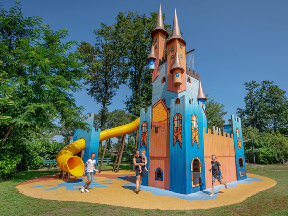 Kleurrijk speelkasteel met een gele glijbaan in de speeltuin van de camping