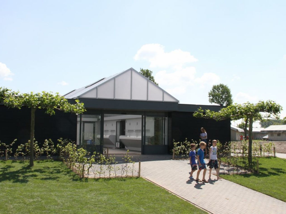 Een gezin wandelt over een pad op het ruim opgezette Vakantiepark Eiland van Maurik, langs een moderne vakantiewoning.