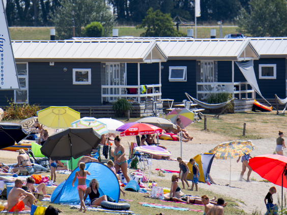 Zonnige dag op het zandstrand voor de vakantiehuisjes op Vakantiepark Eiland van Maurik, vol met badgasten.