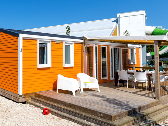 Een vrolijk, oranje gekleurd vakantiechalet met een ruime houten veranda en tuinmeubilair op Vakantiepark Eiland van Maurik.