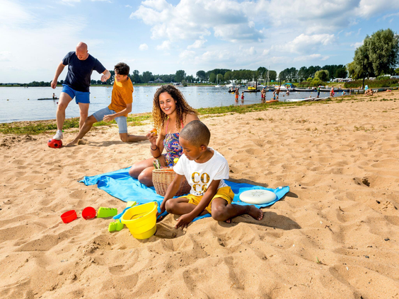 Een gezin speelt met zandspeelgoed op het brede zandstrand aan de recreatieplas van Vakantiepark Eiland van Maurik.