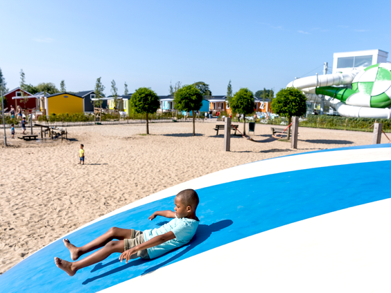 Een meisje ligt te relaxen op de grote blauwe airtrampoline die op het strand van Vakantiepark Eiland van Maurik ligt.