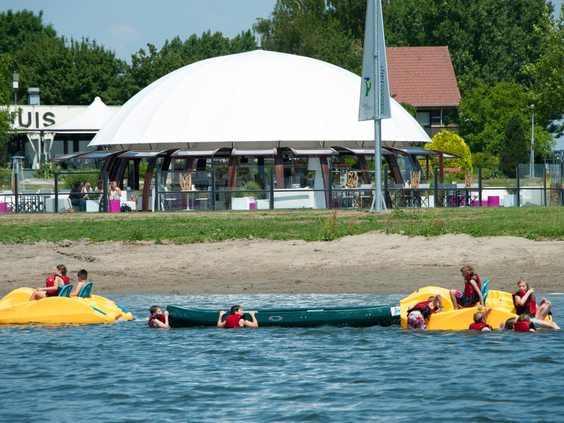 Kinderen klimmen en klauteren op de opblaasbare speeltoestellen van het aquapark in de recreatieplas bij Vakantiepark Eiland van Maurik.