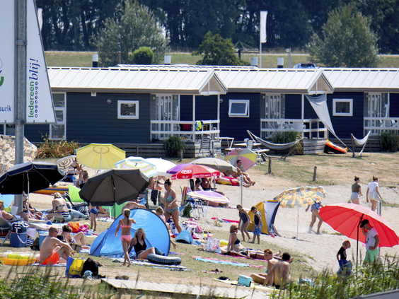 Vakantiegasten genieten op het drukke zandstrand direct voor de vakantiechalets op Vakantiepark Eiland van Maurik.