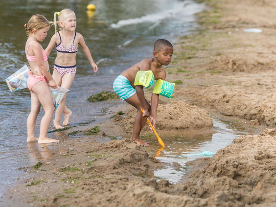 Drie jonge kinderen spelen met zand en water aan de oever van de recreatieplas op Vakantiepark Eiland van Maurik.