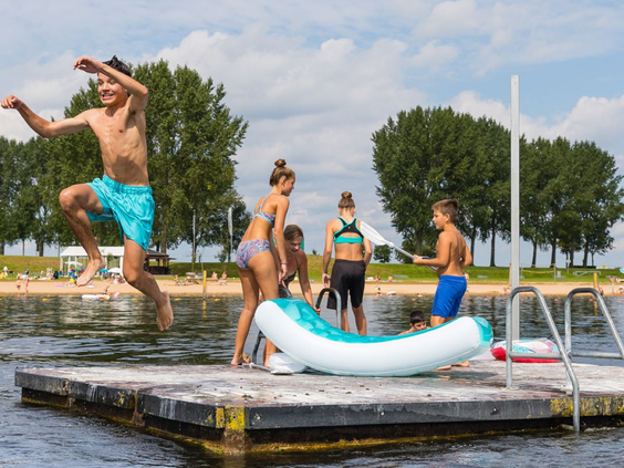 Kinderen springen van een zwemvlot de recreatieplas in op een zonnige dag bij Vakantiepark Eiland van Maurik.