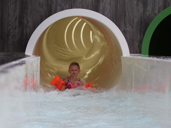 Jong meisje met zwemvleugels komt met een plons uit de waterglijbaan in het binnenzwembad van Vakantiepark Eiland van Maurik.