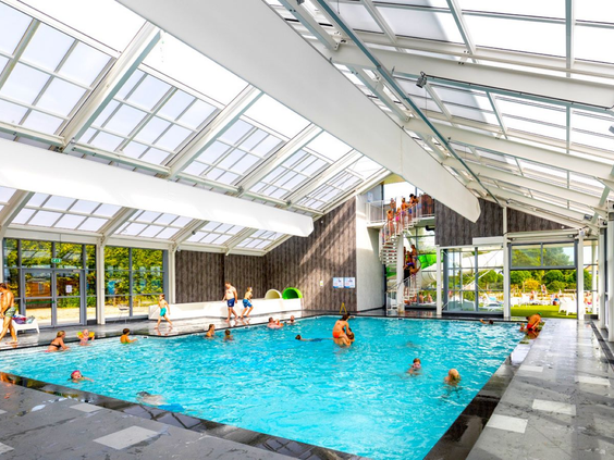 Het overdekte zwembad met schuifbaar dak op Vakantiepark Eiland van Maurik, waar gasten zwemmen en van de glijbaan gaan.