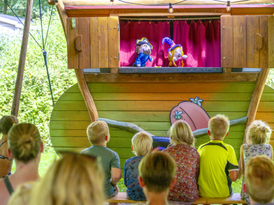 Kinderen kijken aandachtig naar een poppenkastvoorstelling op de camping